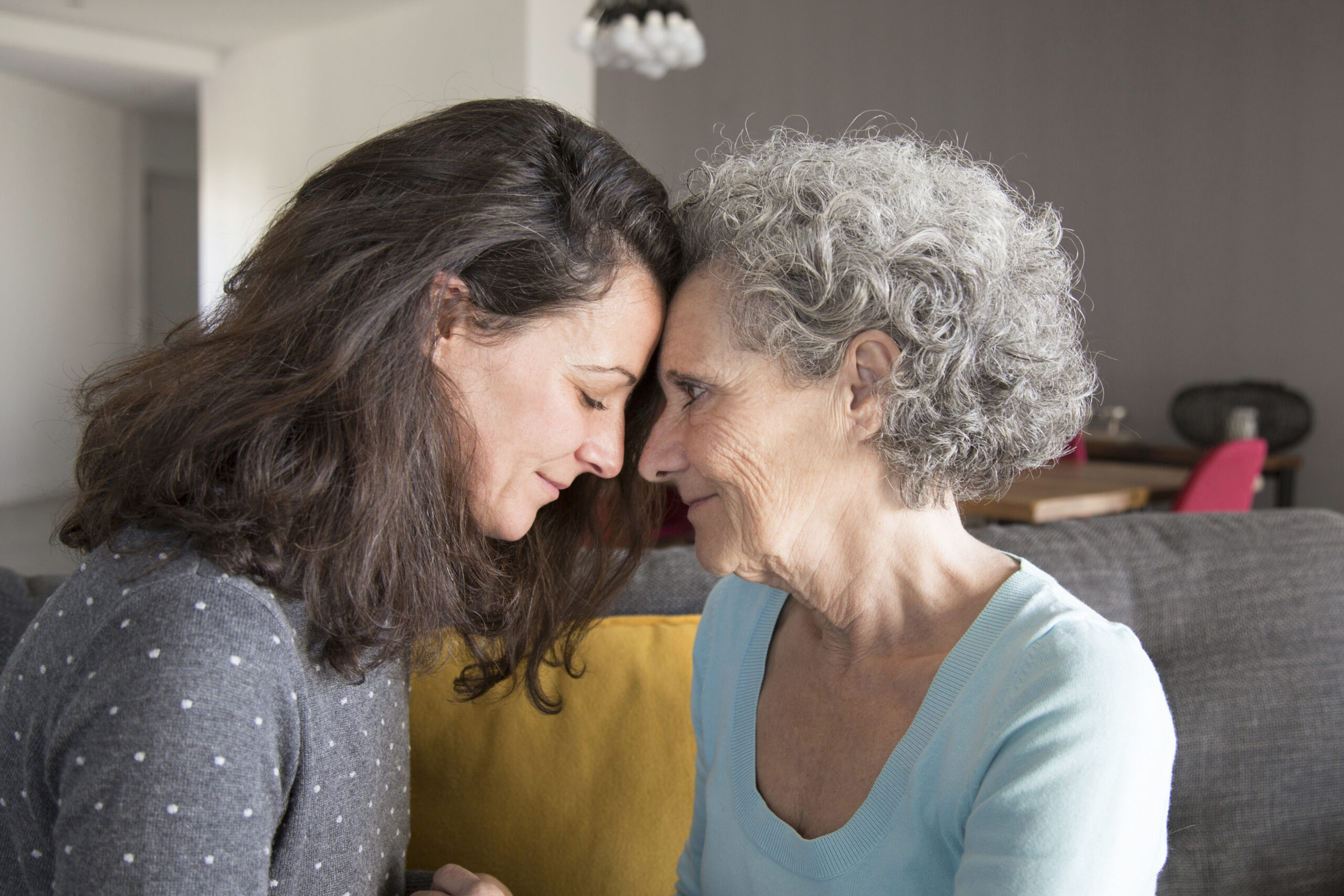 Adult daughter and old mother touching foreheads
